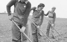 Black and white photo of three land girls pictured with hoes, in a field