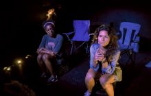 The two actors sit in semi-darkness on folding chairs, looking pensive at the world