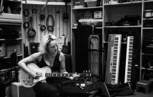 Black and white photo of Biz Lyon playing guitar, in a music room